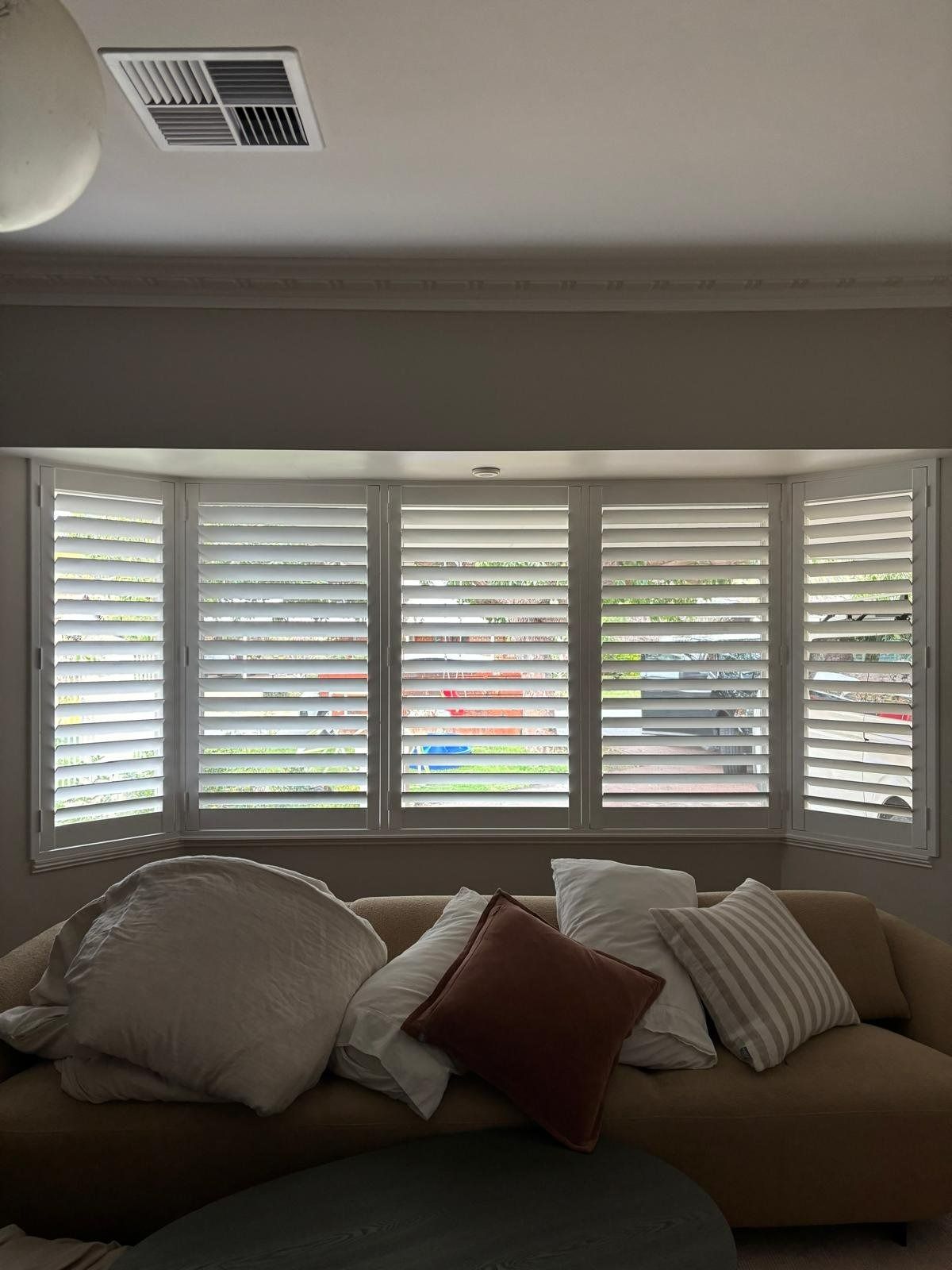 Plantation shutters installed in a living room with bay window shutters and a sofa covered in pillows in Perth, WA.