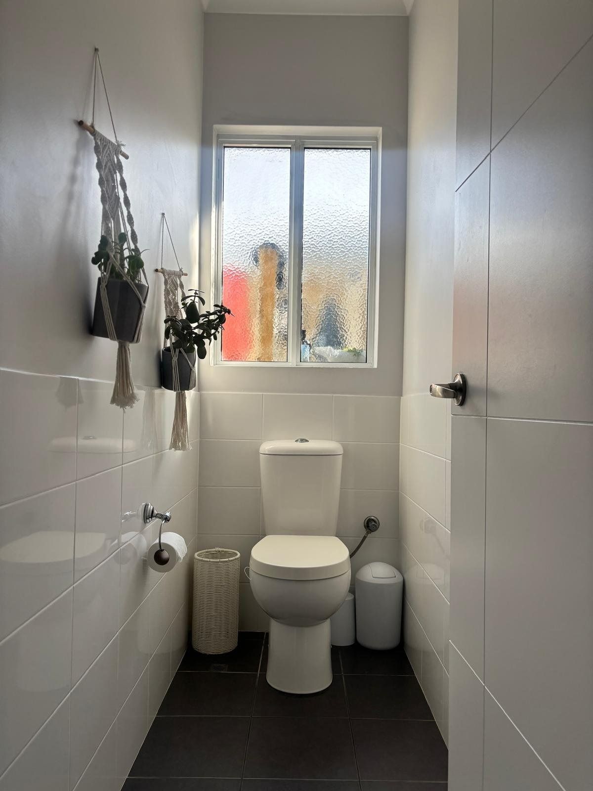 Plantation shutters installed in a narrow white bathroom with a toilet under a frosted window and hanging potted plants in Perth, WA.