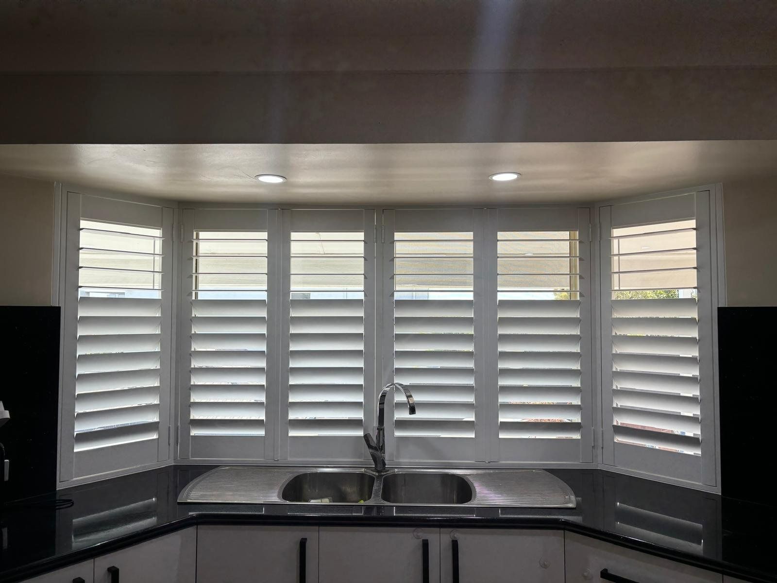 Plantation shutters installed in a kitchen sink beneath white plantation shutters over a wide window in Perth, WA.