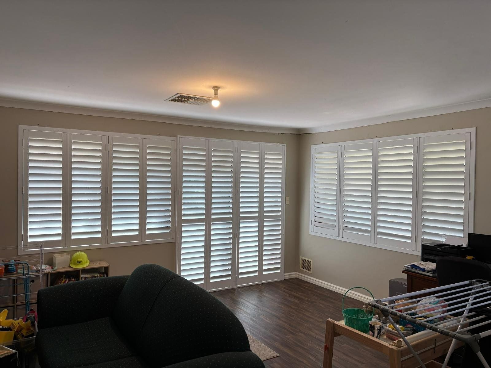 Plantation shutters installed in a bright living room with white plantation shutters, gray walls, and dark wood floors in Perth, WA.