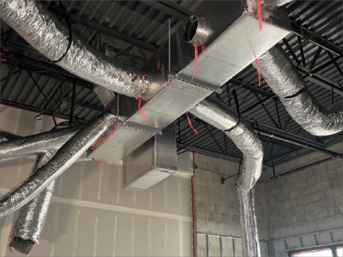 HVAC ductwork installation in a commercial building with exposed metal beams and unfinished walls.