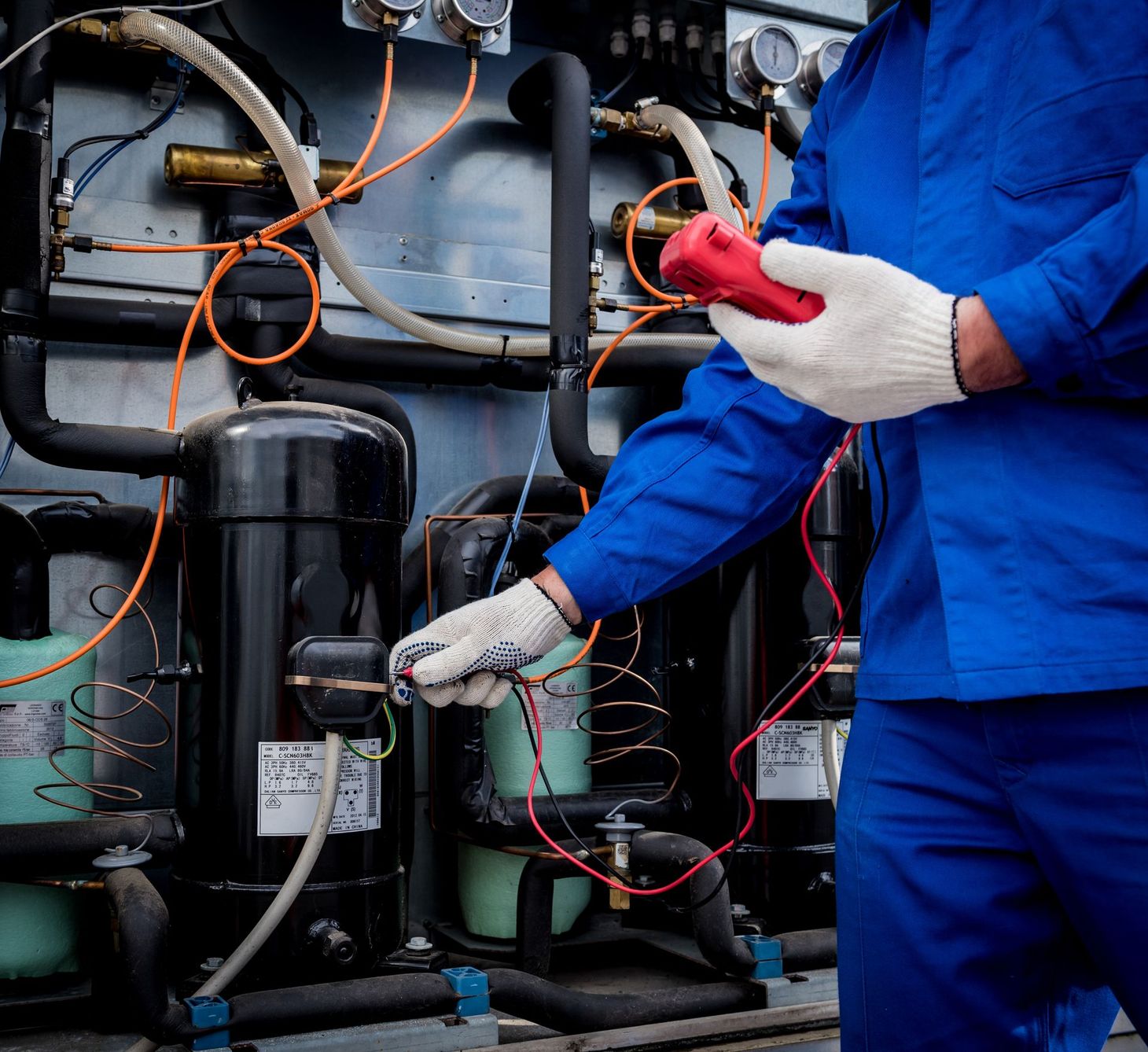 Person in blue jumpsuit testing electrical components with a red multimeter.