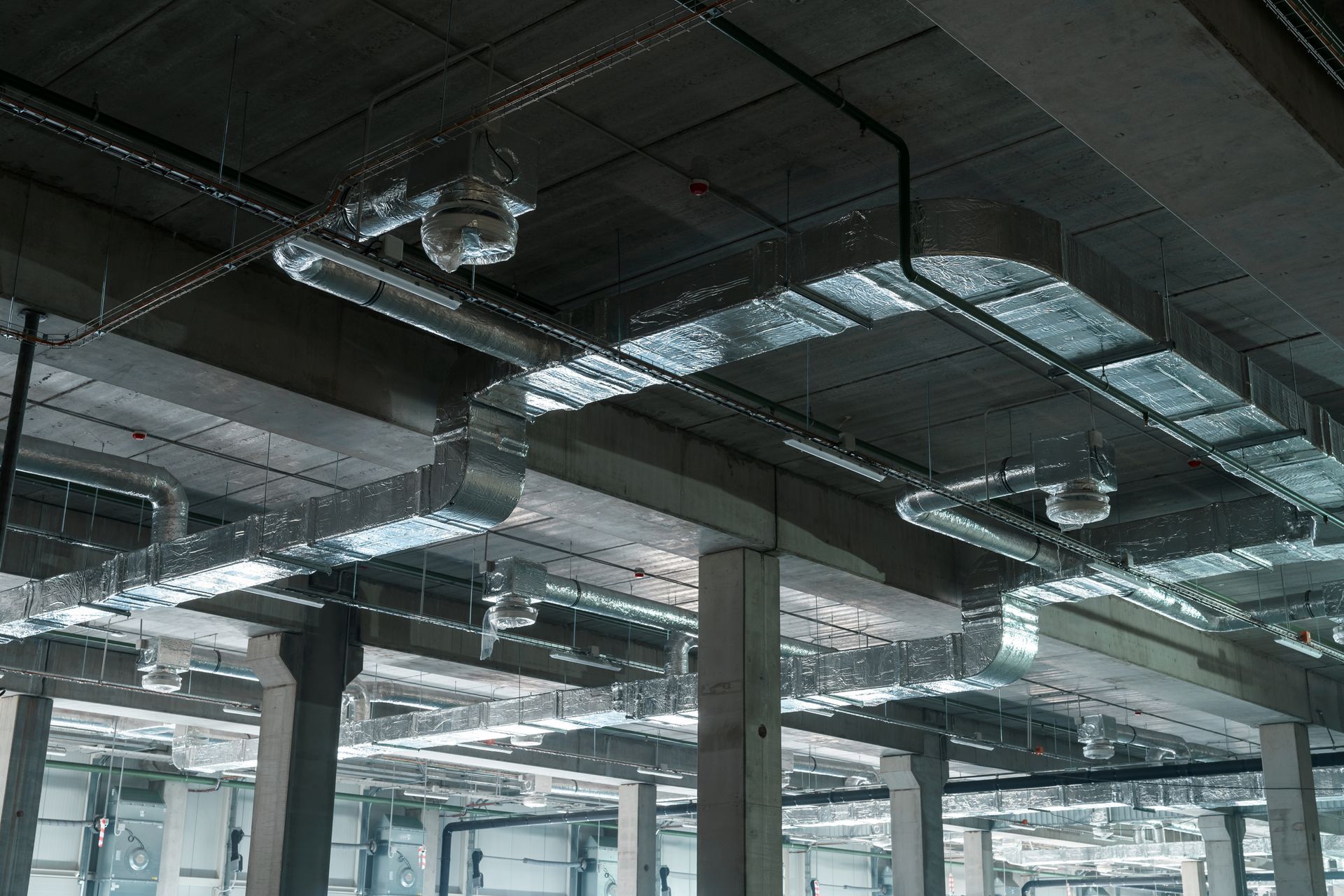 Industrial interior: concrete ceiling with silver ventilation ducts and black electrical conduit.