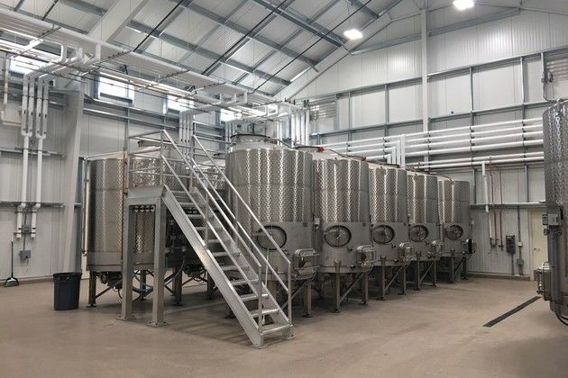 A large warehouse filled with lots of stainless steel tanks and stairs.