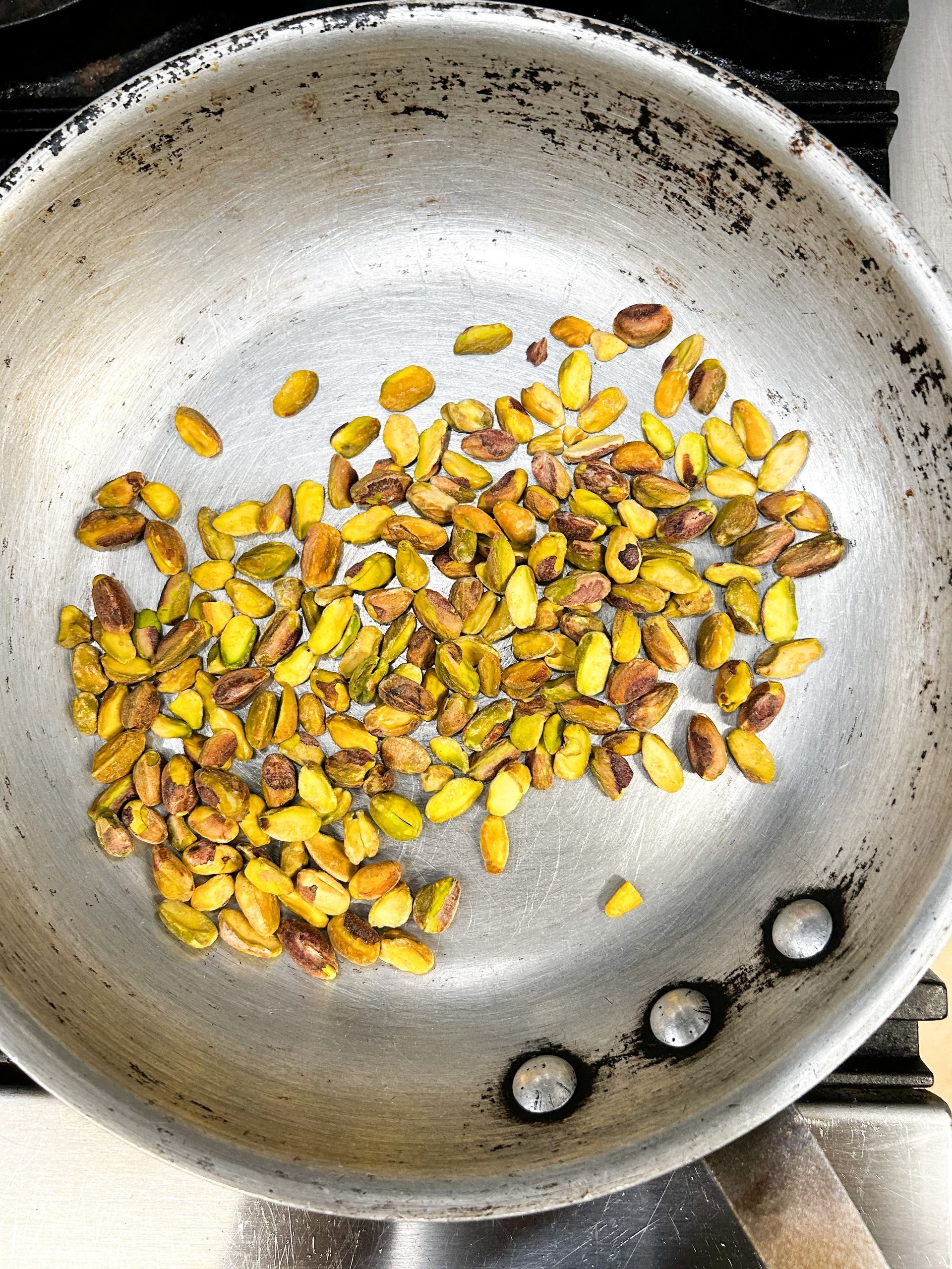 Pistachios are being cooked in a frying pan on a stove.