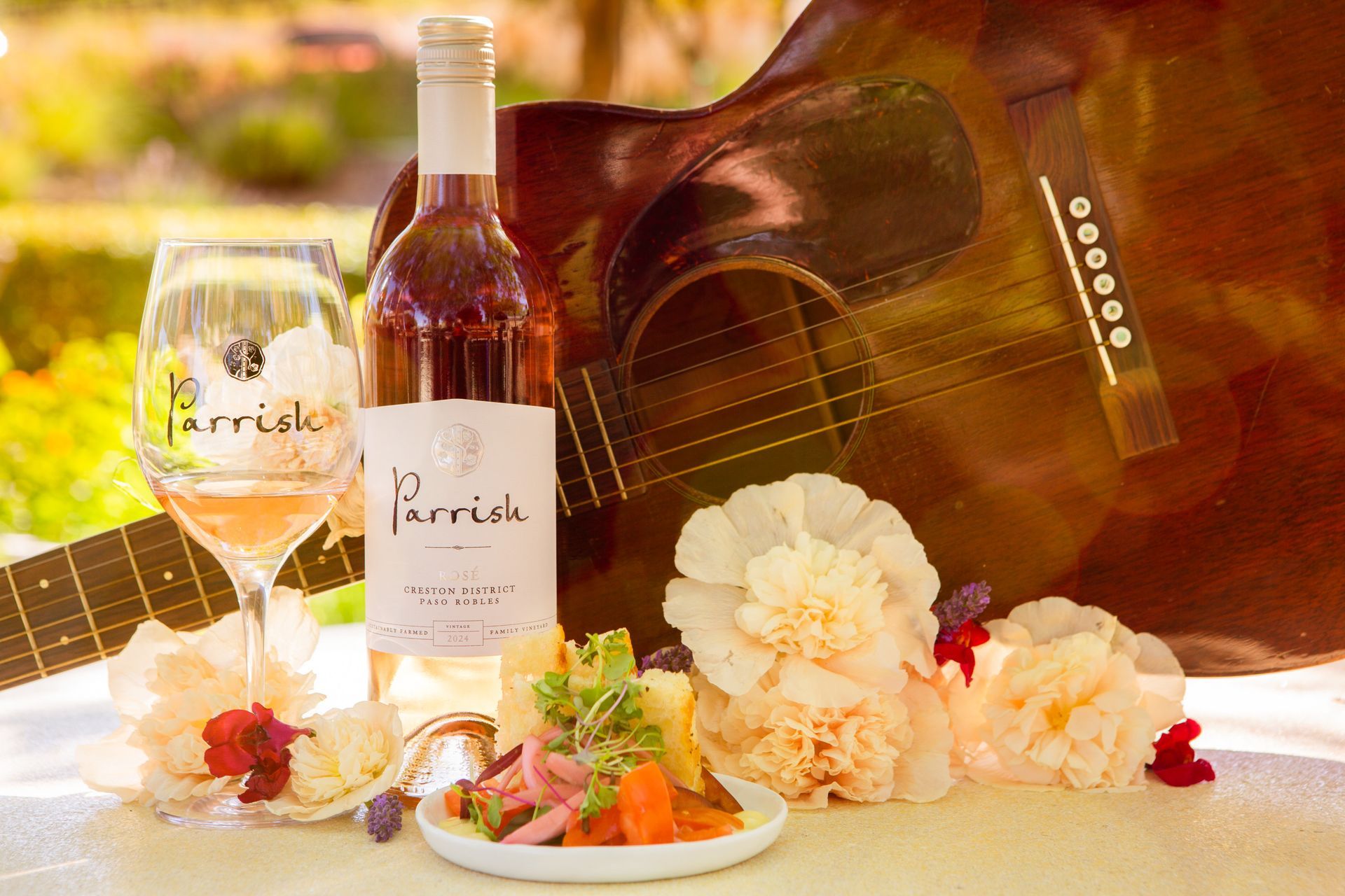A bottle of Parrish Rose wine next to flowers and a guitar.