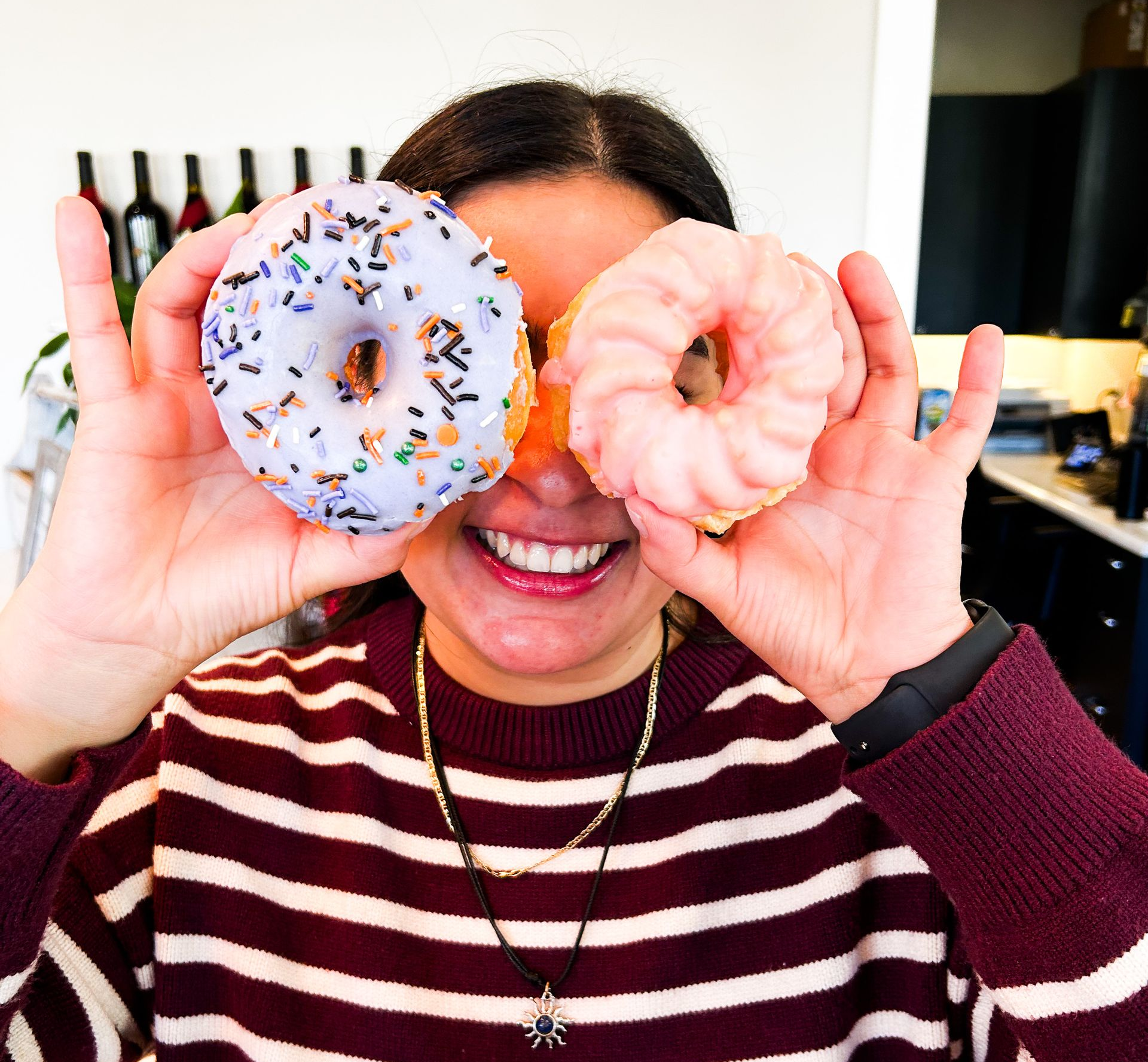 A person holding two donuts in front of their eyes and smiling.