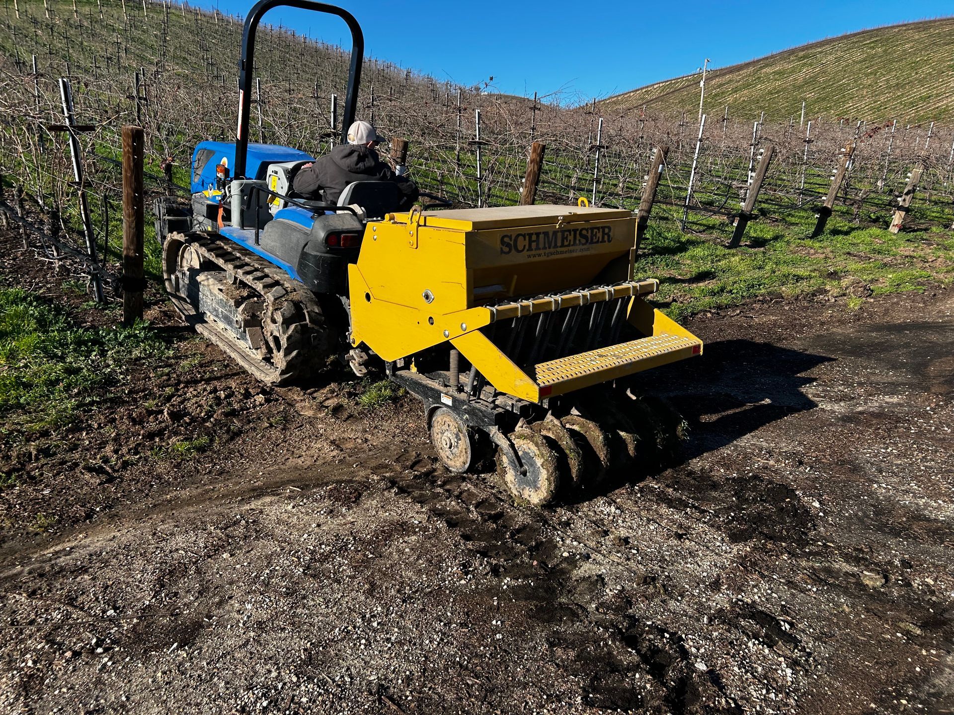 Yellow orchard machine driving through muddy vineyard rows