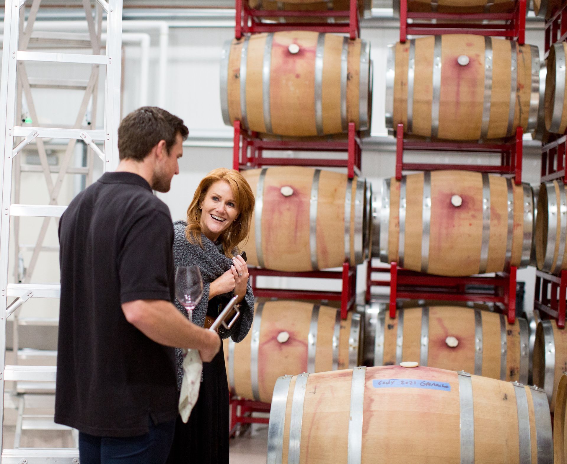 Two people talking in front of the wine barrels.