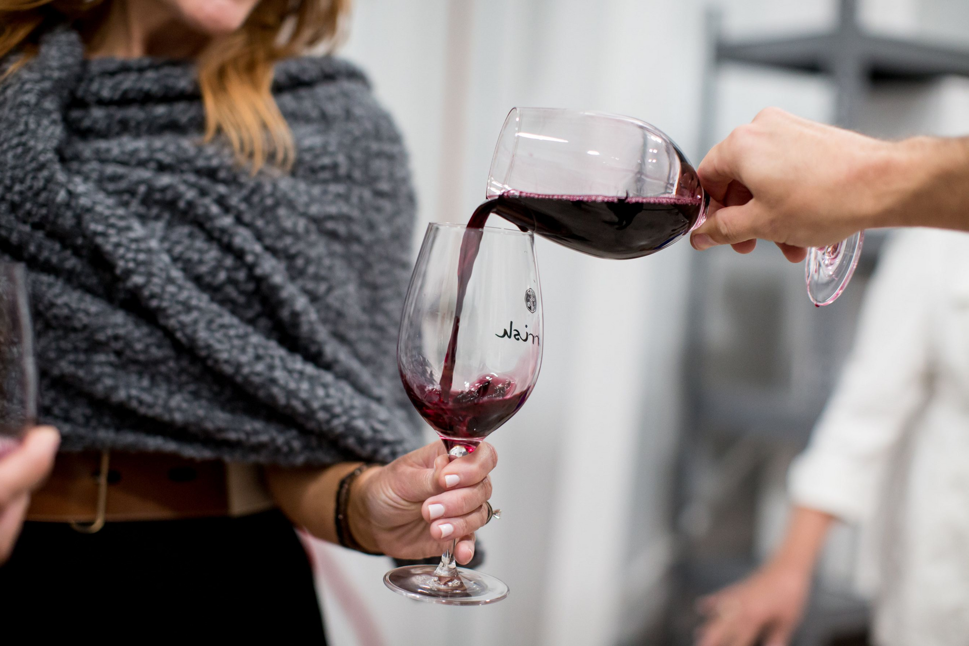 A hand pouring red wine from one glass to another during a Parrish Family Vineyard barrel room tour.