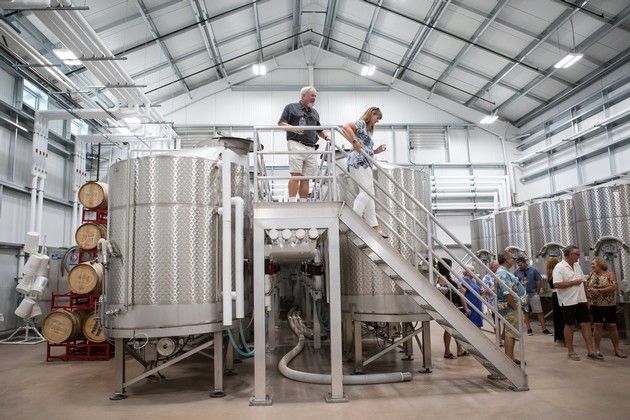 A group of people walking next to wine tanks. 