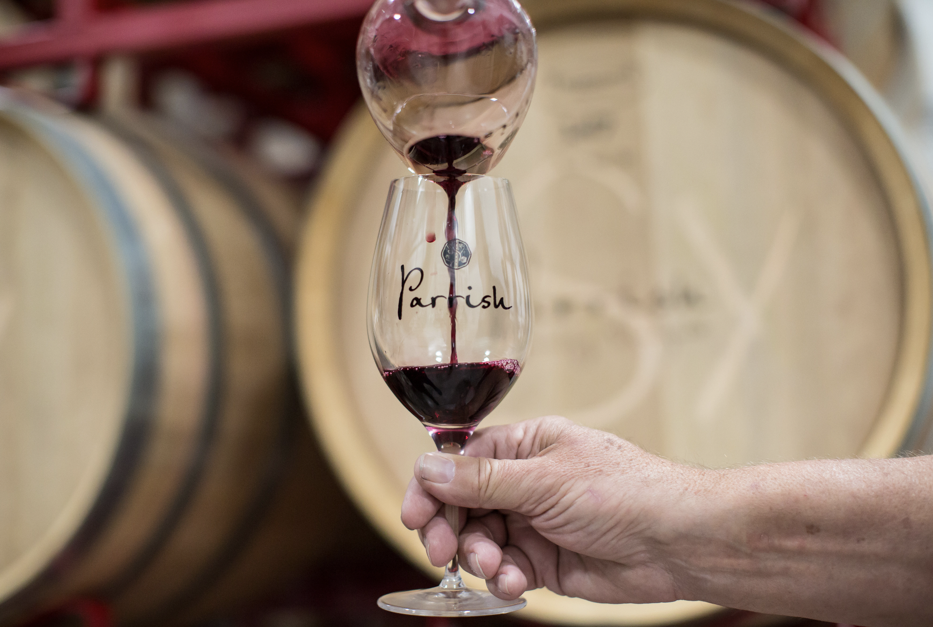Red wine being poured into a Parrish glass in front of a wine barrel.