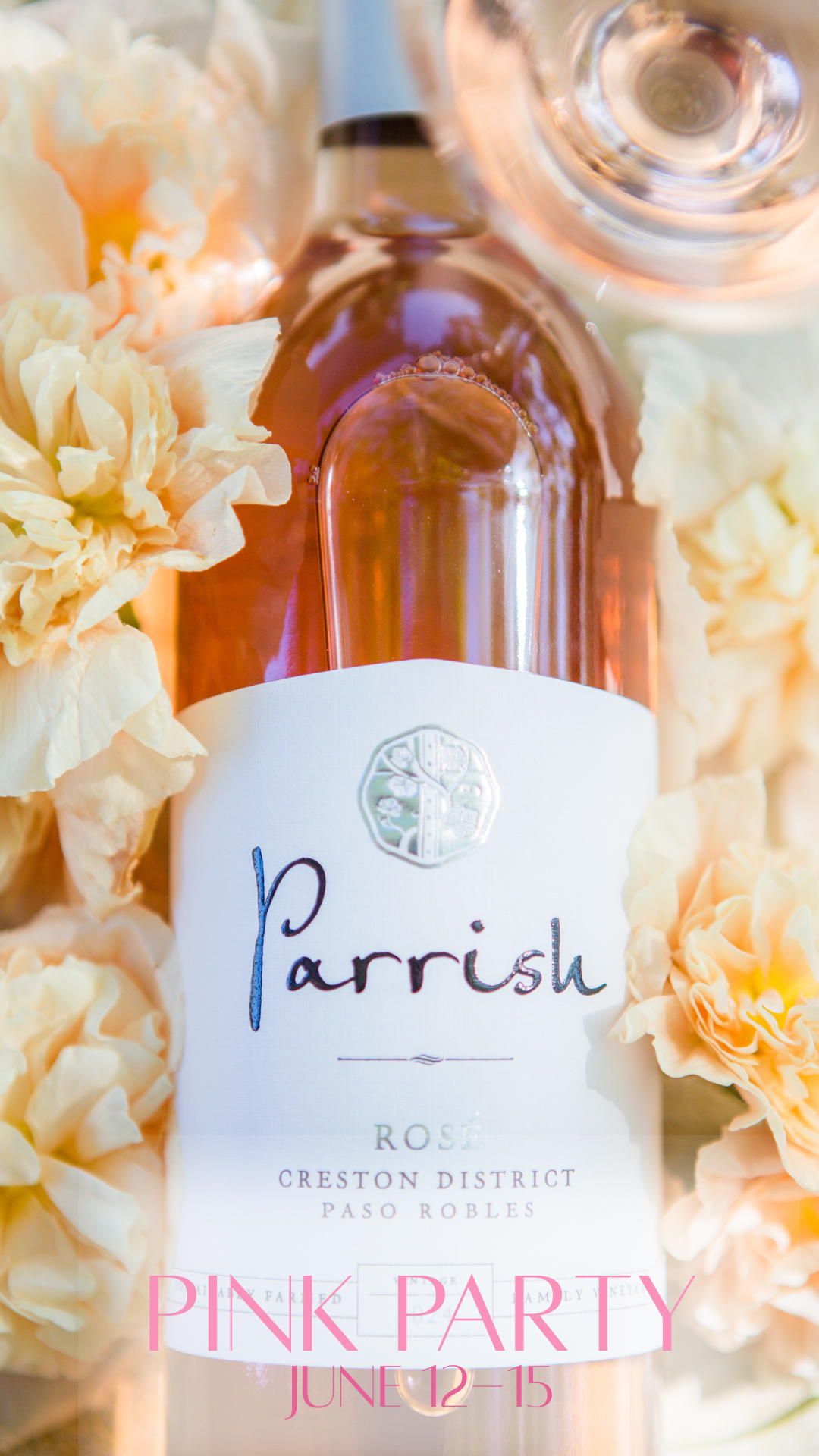A close up of a bottle of rose next to a wine glass and flowers.