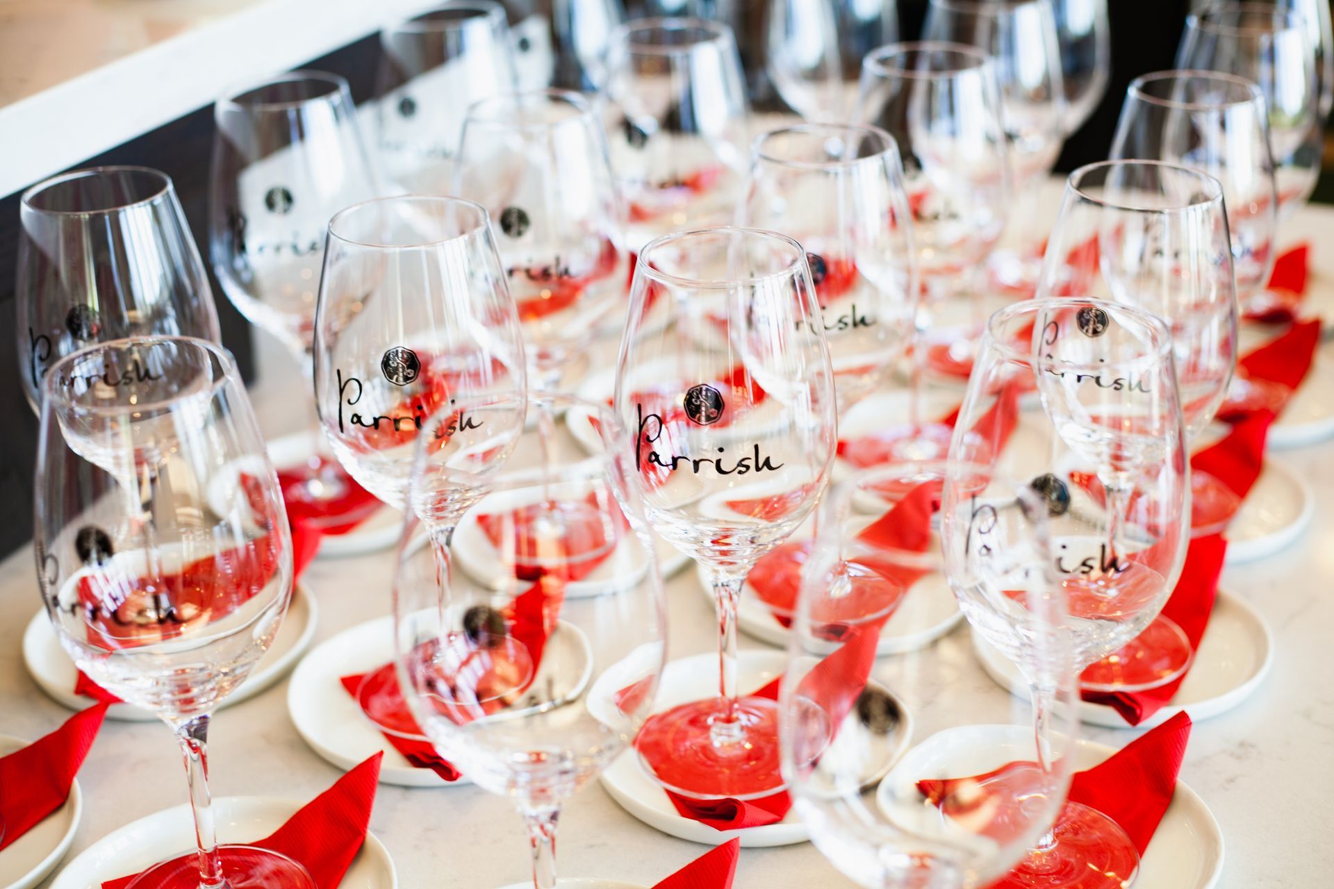 Parrish Family Vineyard branded wine glasses arranged on a table atop coasters and red cocktail napkins.