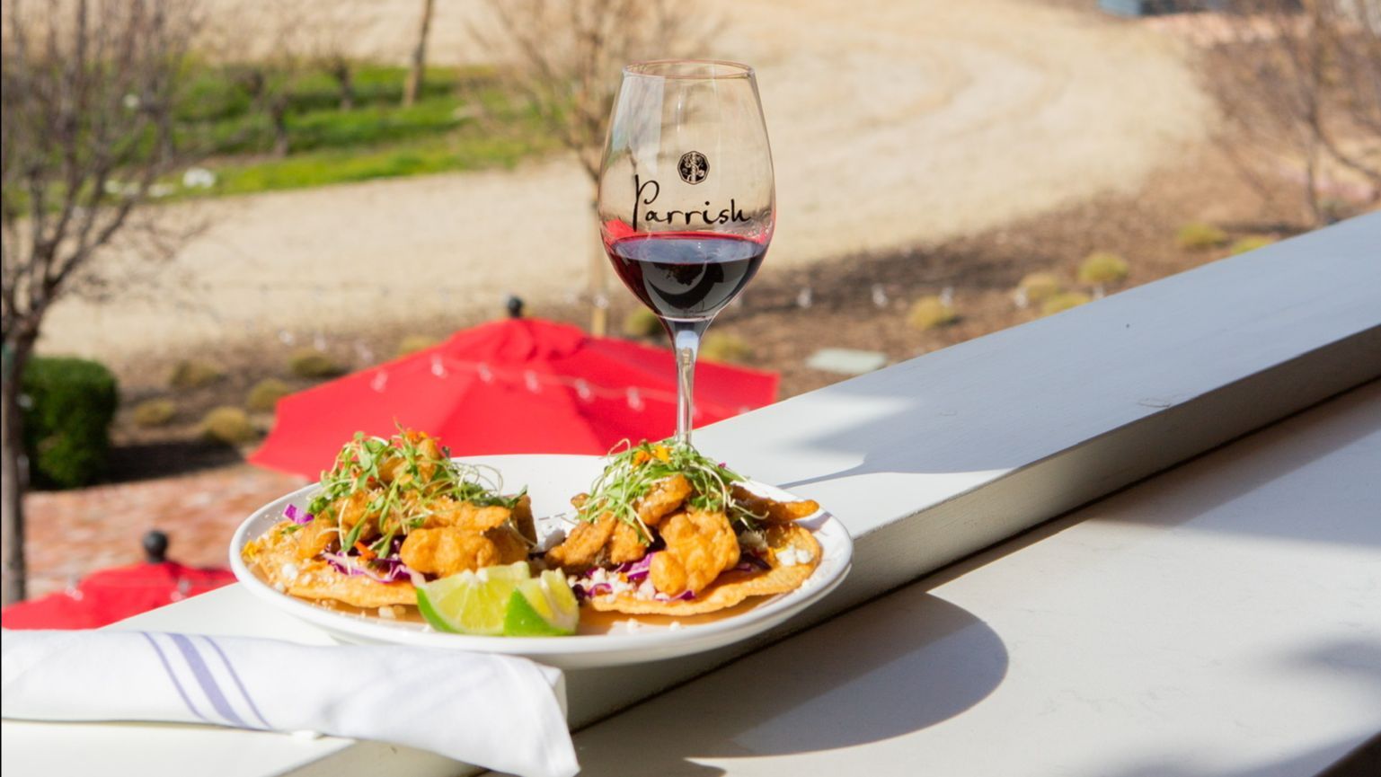 A glass of a Parrish red wine with a plate of tacos.