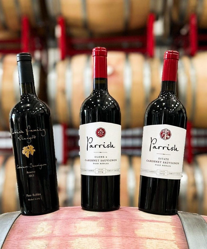Bottles of red wine in front of wine barrels.