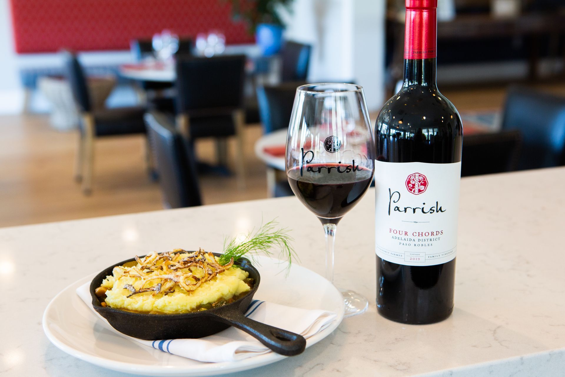 A bottle of wine and a glass of wine are on a table next to a plate of food.