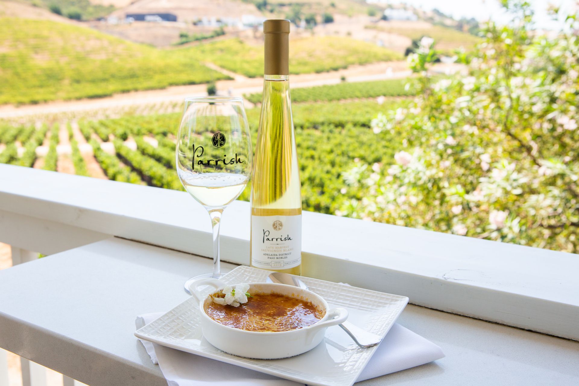 A bottle of white wine, a filled glass, and a plate of food are on a table.
