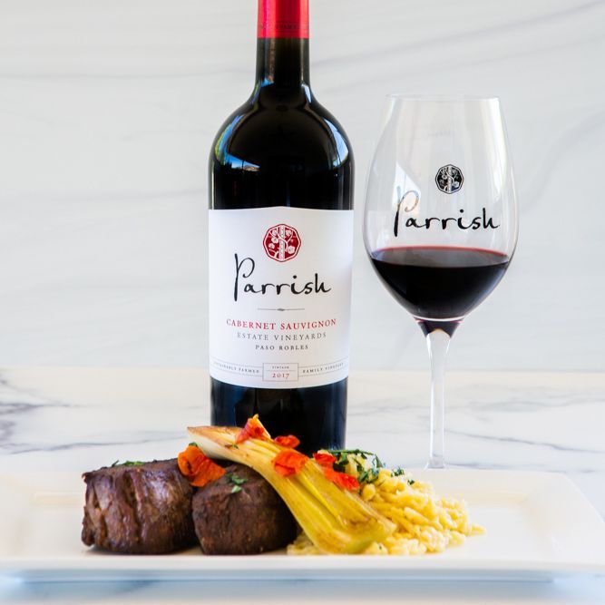 A bottle of Parrish Cabernet Sauvignon next to a glass of wine.