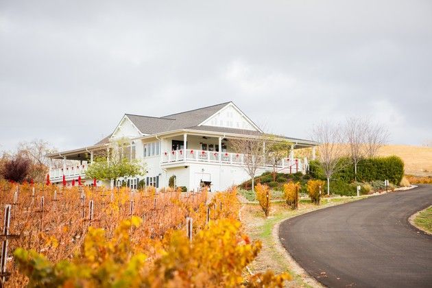 A white house is sitting on the side of a road next to a vineyard.