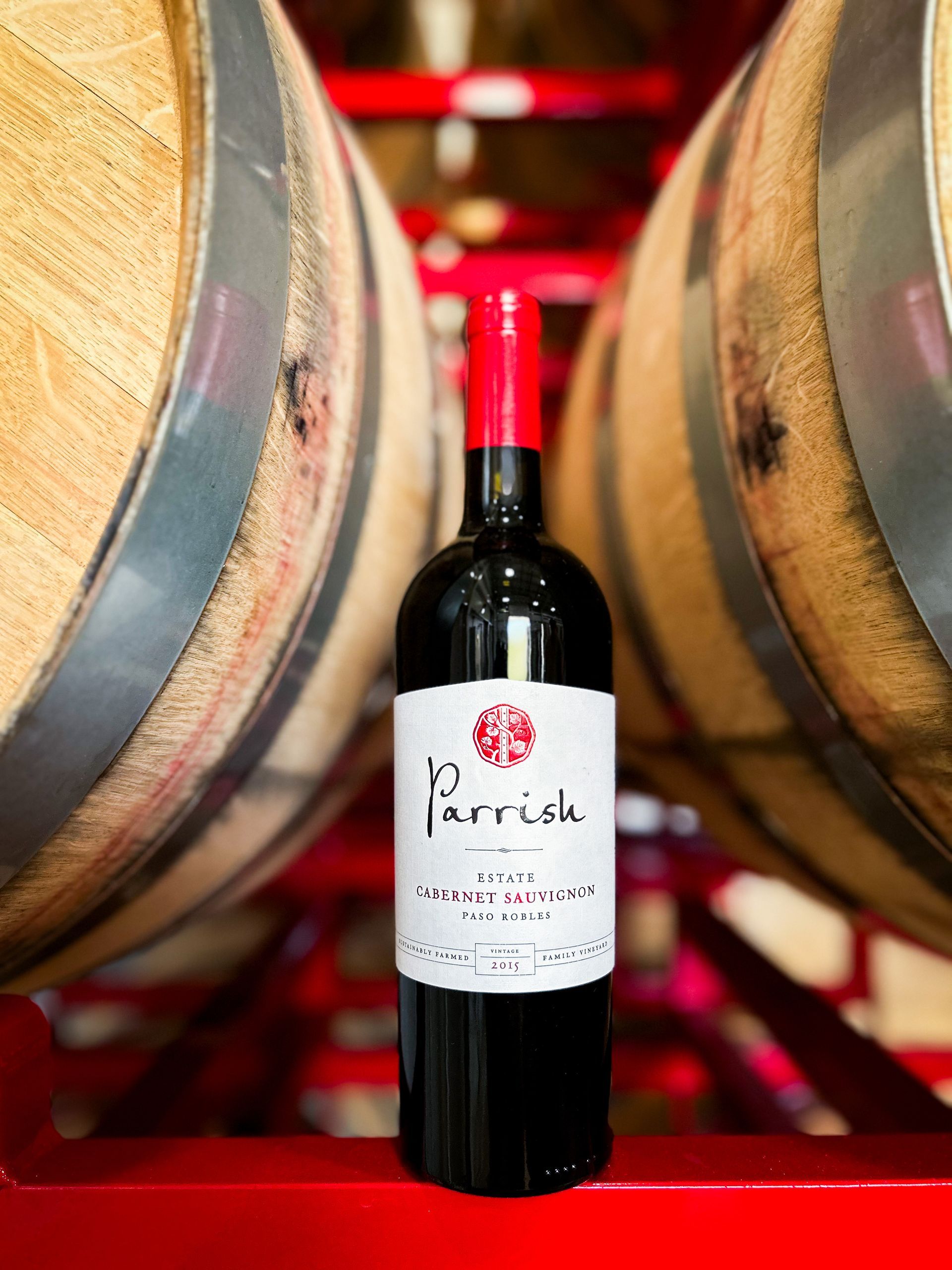 A bottle of Parrish Cabernet Sauvignon in front of wine barrels.