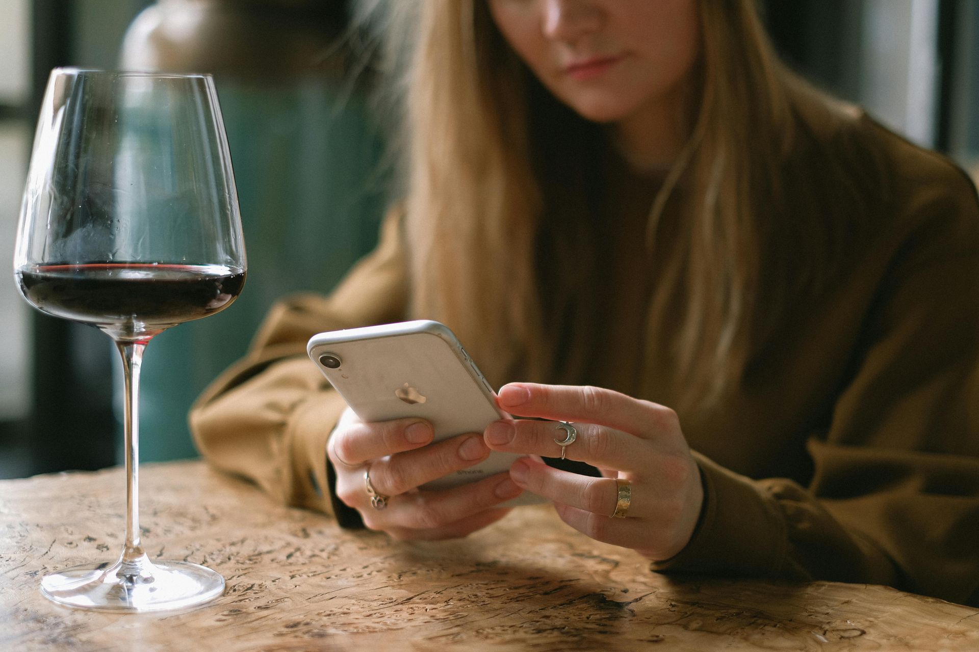 Person using a smartphone at a table beside a glass of red wine