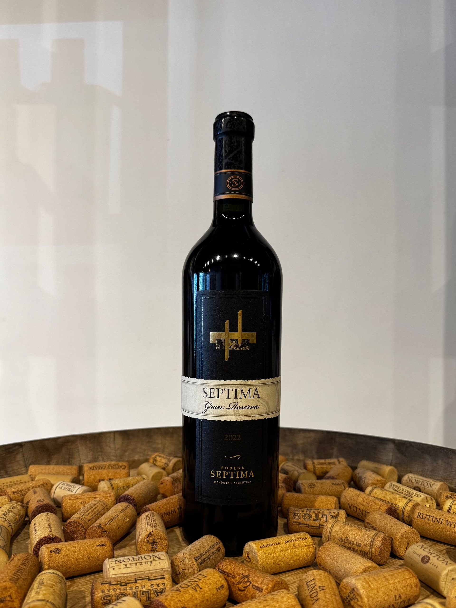 Una botella de vino tinto con etiqueta dorada y tapón negro, rodeada de corchos.