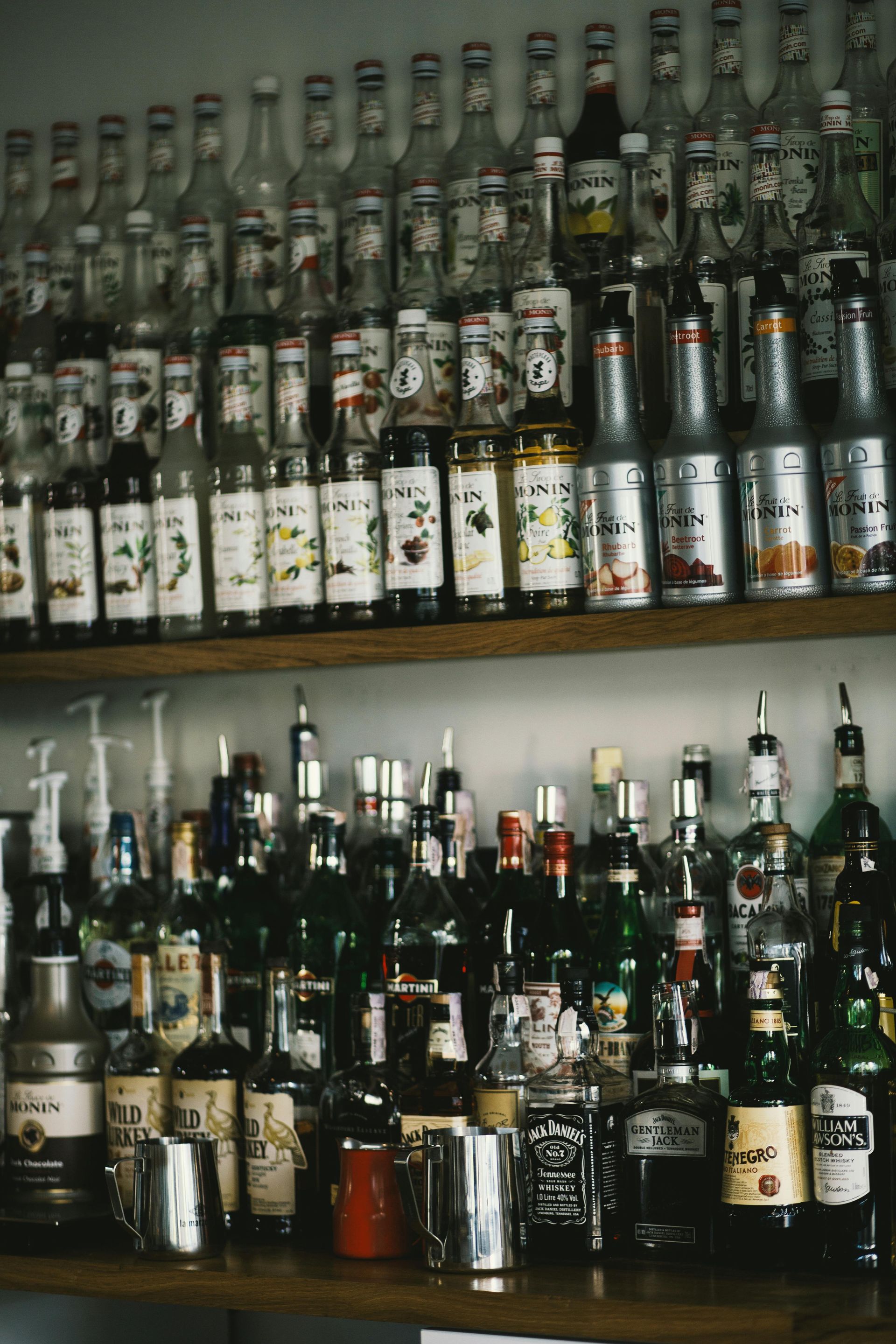 Estantes repletos de botellas de licor variadas en un mostrador de bar con iluminación tenue.