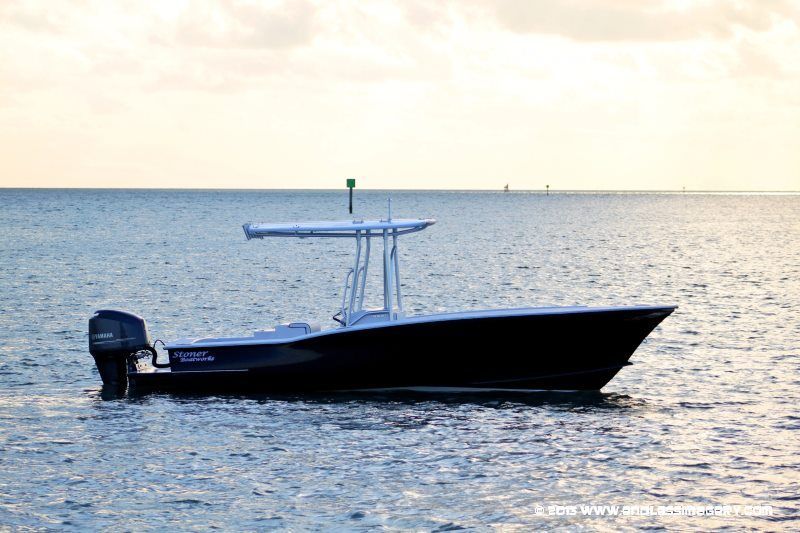 A black center console boat with a T-top motorboat cruises on calm water during a sunset.