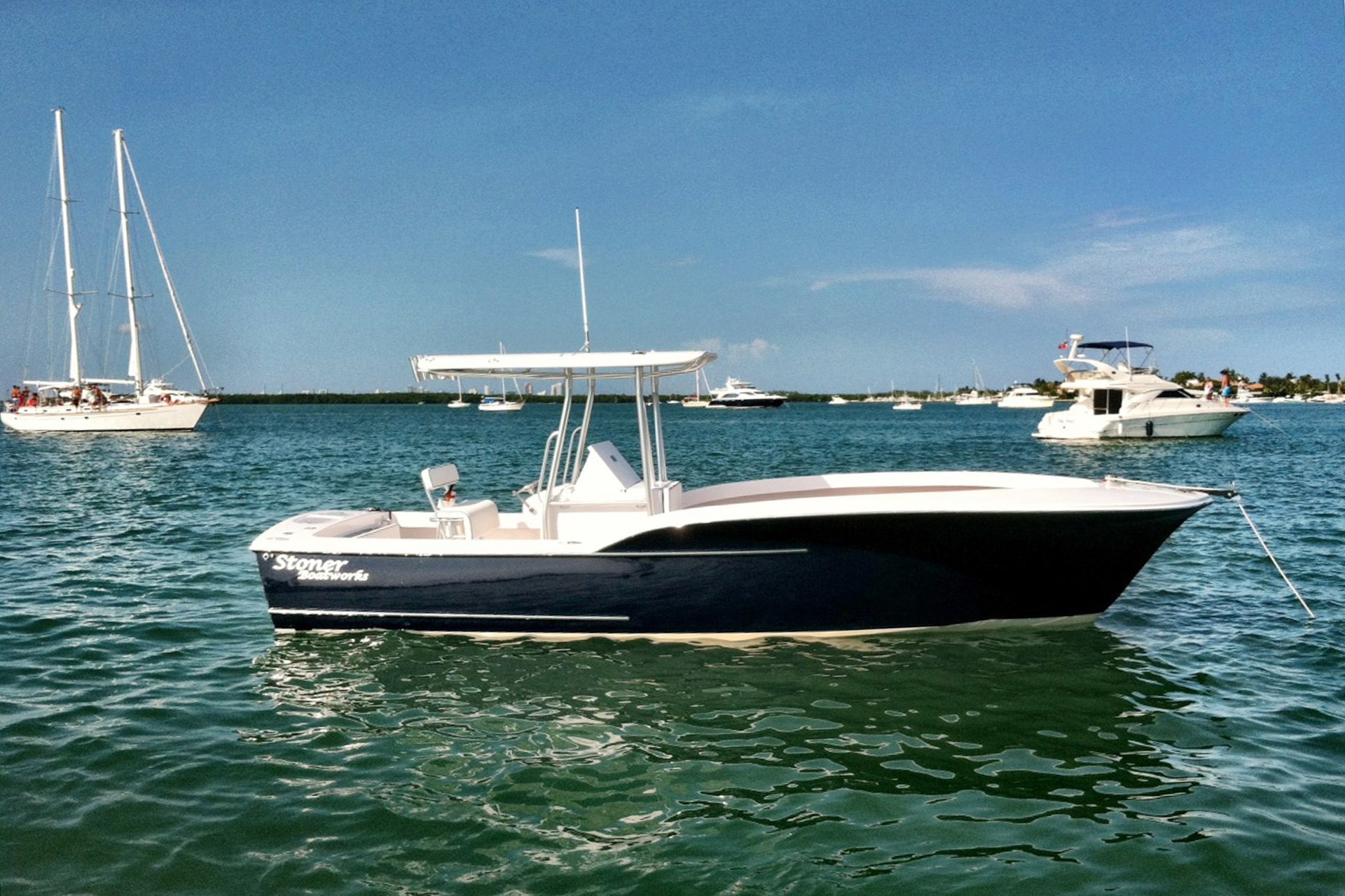 A dark blue and white center console boat anchored in calm coastal waters, with other boats visible in the distance.