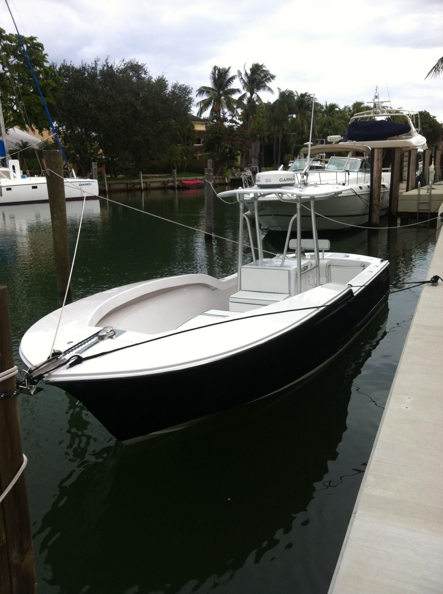 A black and white center console boat tied to a wooden dock in a canal lined with palm trees and other vessels.