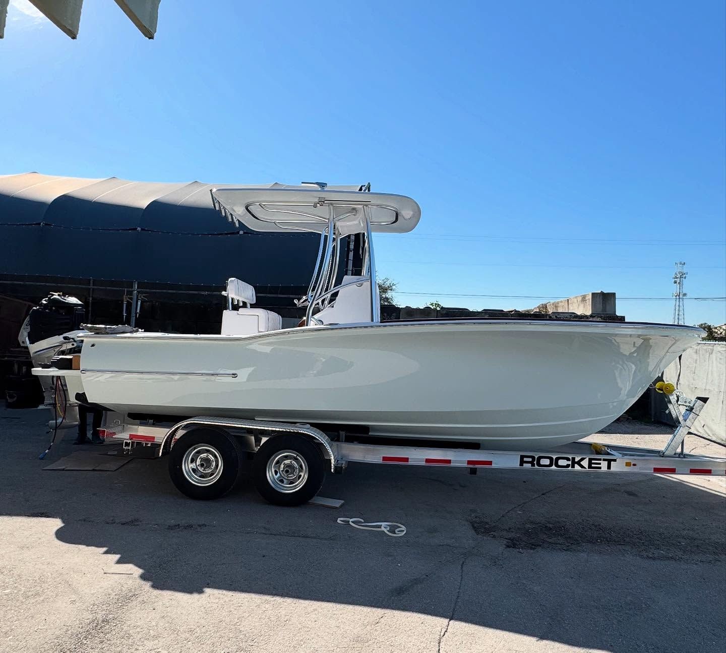 A white center console boat on a Rocket boat trailer, parked on a paved lot under a clear blue sky.