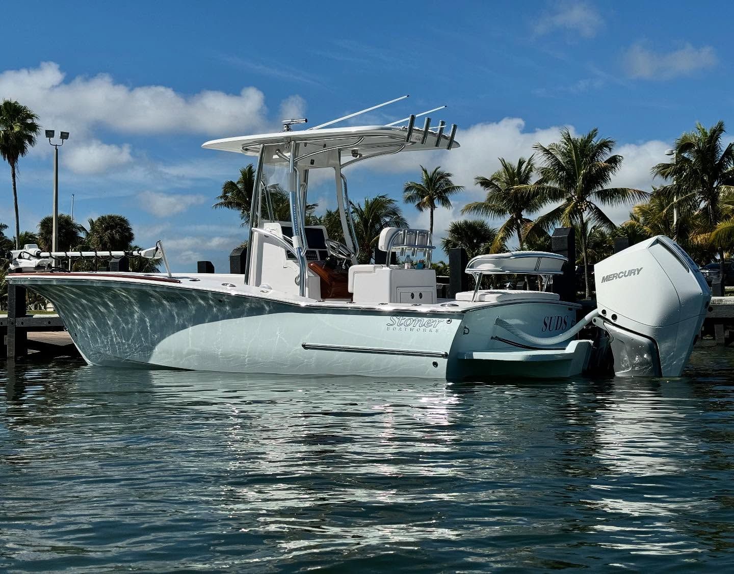 Light blue center console fishing boat with a white outboard motor, moored at a dock under a bright, sunny sky.