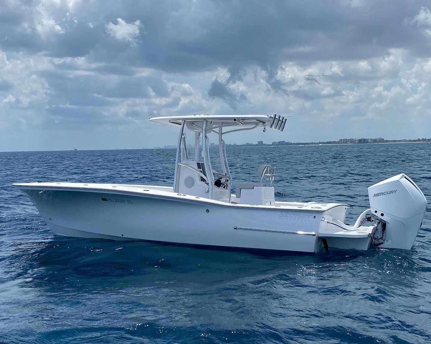 A white center console motorboat with a T-top cruising on deep blue ocean water under a cloudy sky.