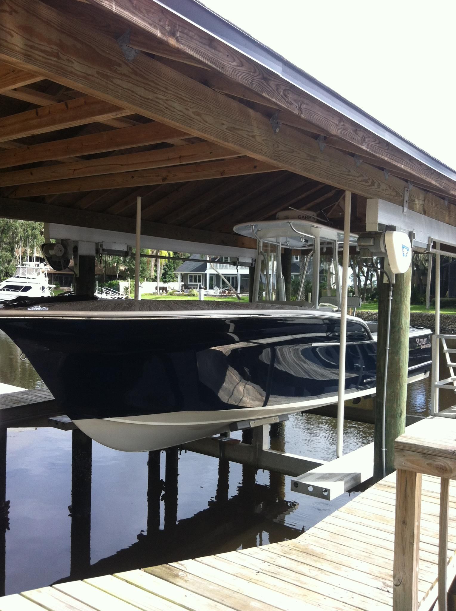 A dark blue motorboat hoisted on a mechanical lift under a wooden covered boat slip at a dock.