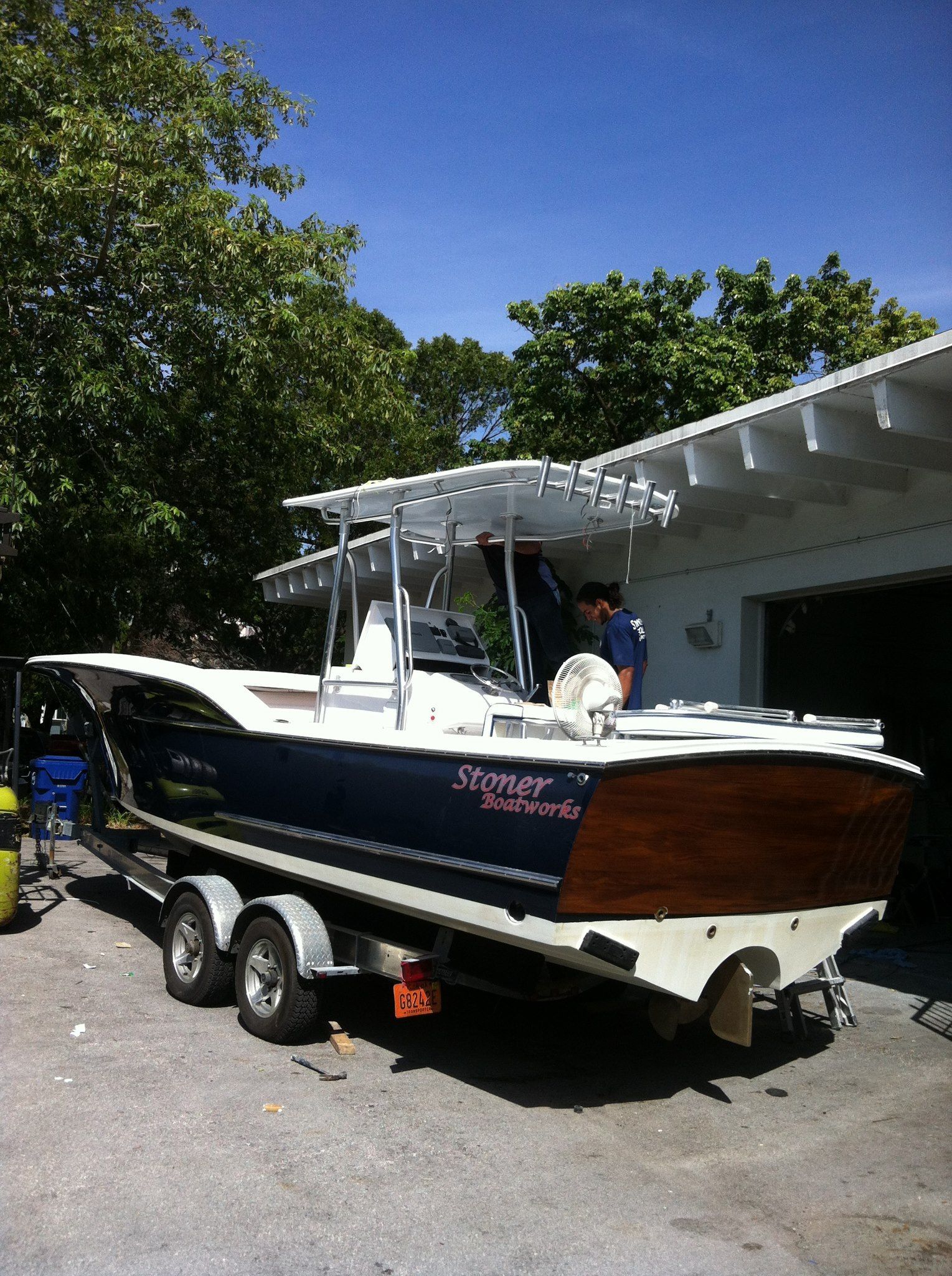 A dark blue and wood-paneled center console boat on a trailer parked outside a building under a clear blue sky.