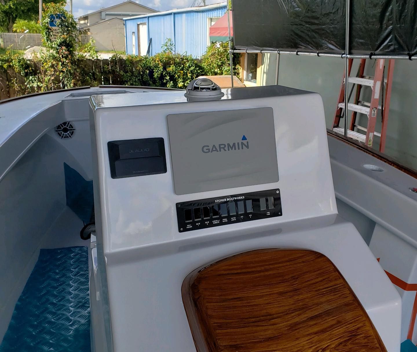 A white boat center console featuring a Garmin GPS screen, a row of black switches, and a wooden seat.