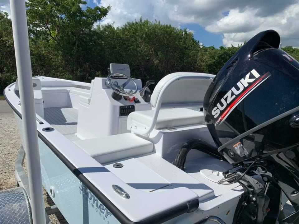 A light blue boat with a white interior and a Suzuki outboard motor, parked on a trailer in a sunny outdoor setting.