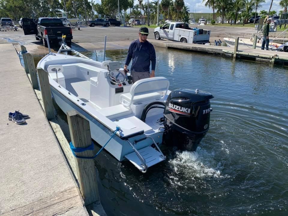 A person steers a white motorboat with a black Suzuki engine away from a concrete boat ramp dock.