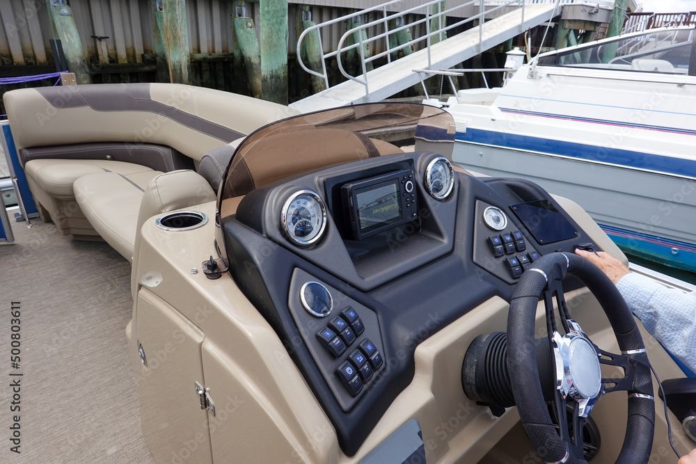 A person is driving a pontoon boat at a dock.
