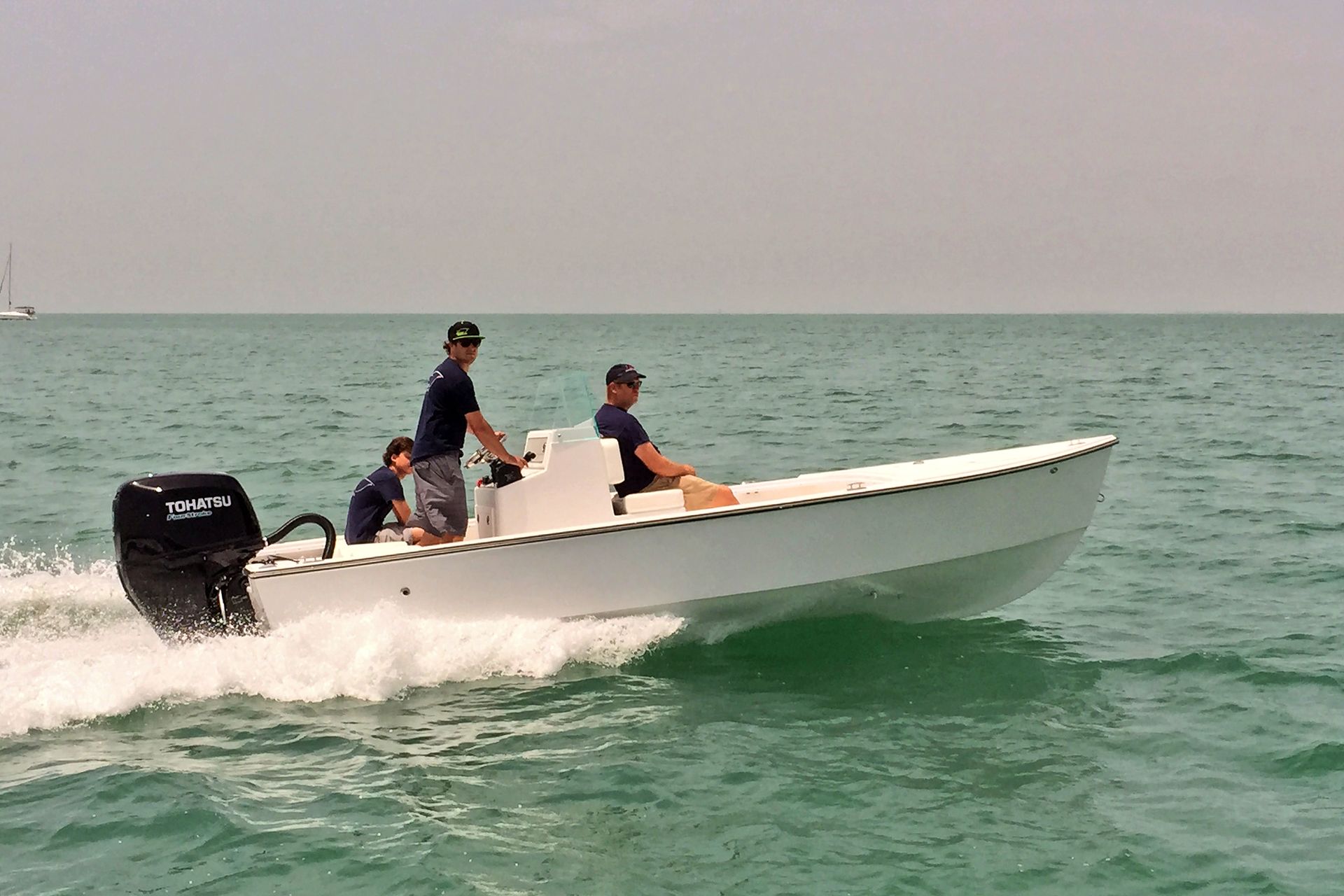Three people riding in a small white motorboat on the ocean.