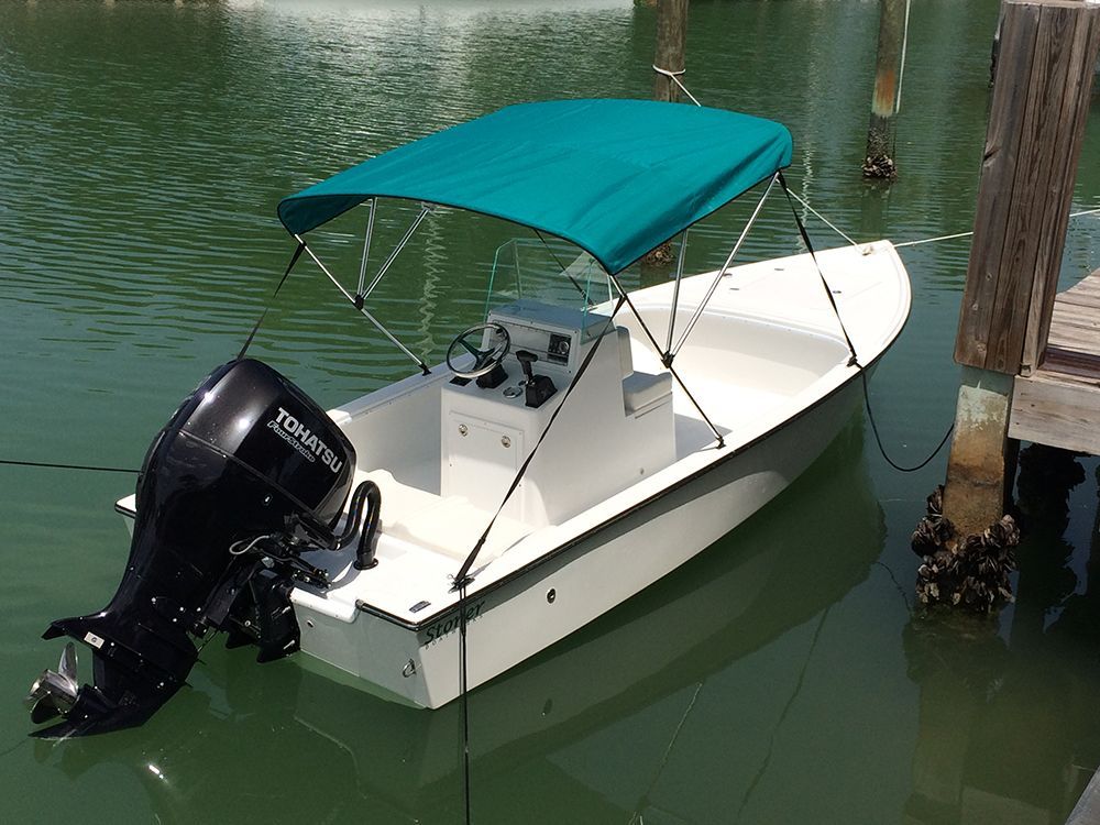 A small white motorboat with a teal canvas top docked at a wooden pier in calm, green water.