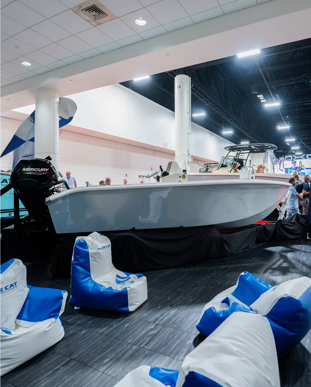 A white boat on display indoors with several blue and white beanbag chairs arranged in front of it on a dark floor.