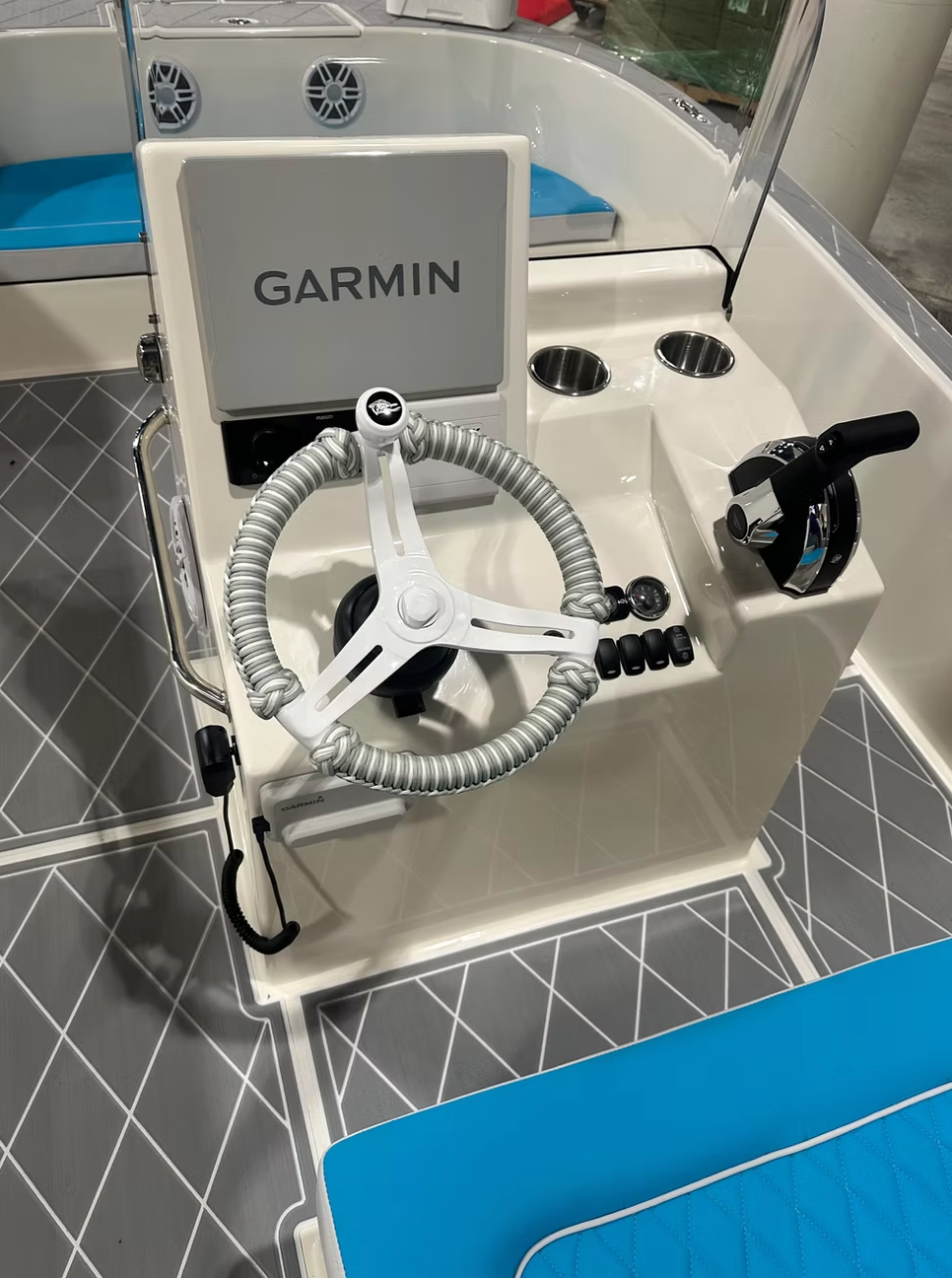 Boat helm station with a Garmin navigation screen, white steering wheel, throttle control, and teal blue seating.