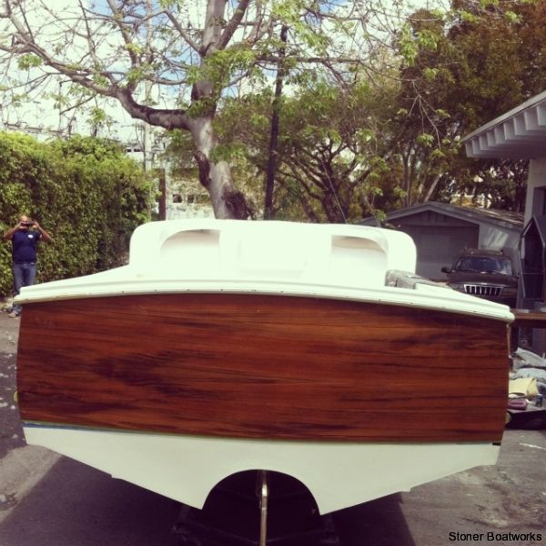 The rear view of a boat under restoration, featuring a varnished wooden transom and a fresh white hull, outdoors.
