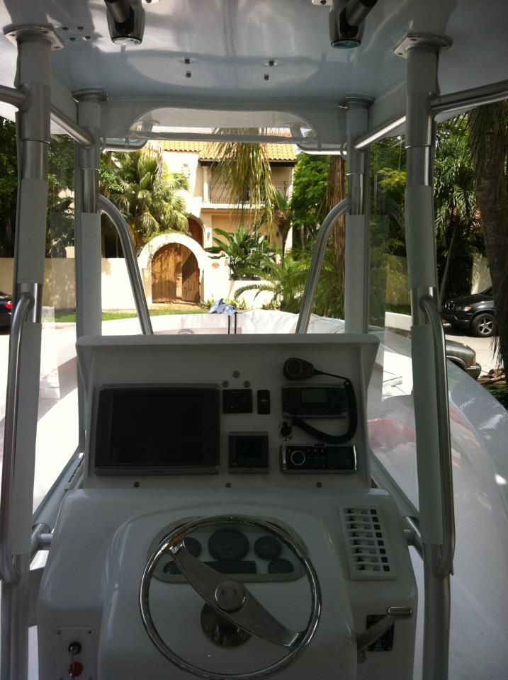 The cockpit of a boat featuring a steering wheel, navigation screen, and radio controls under a T-top canopy.