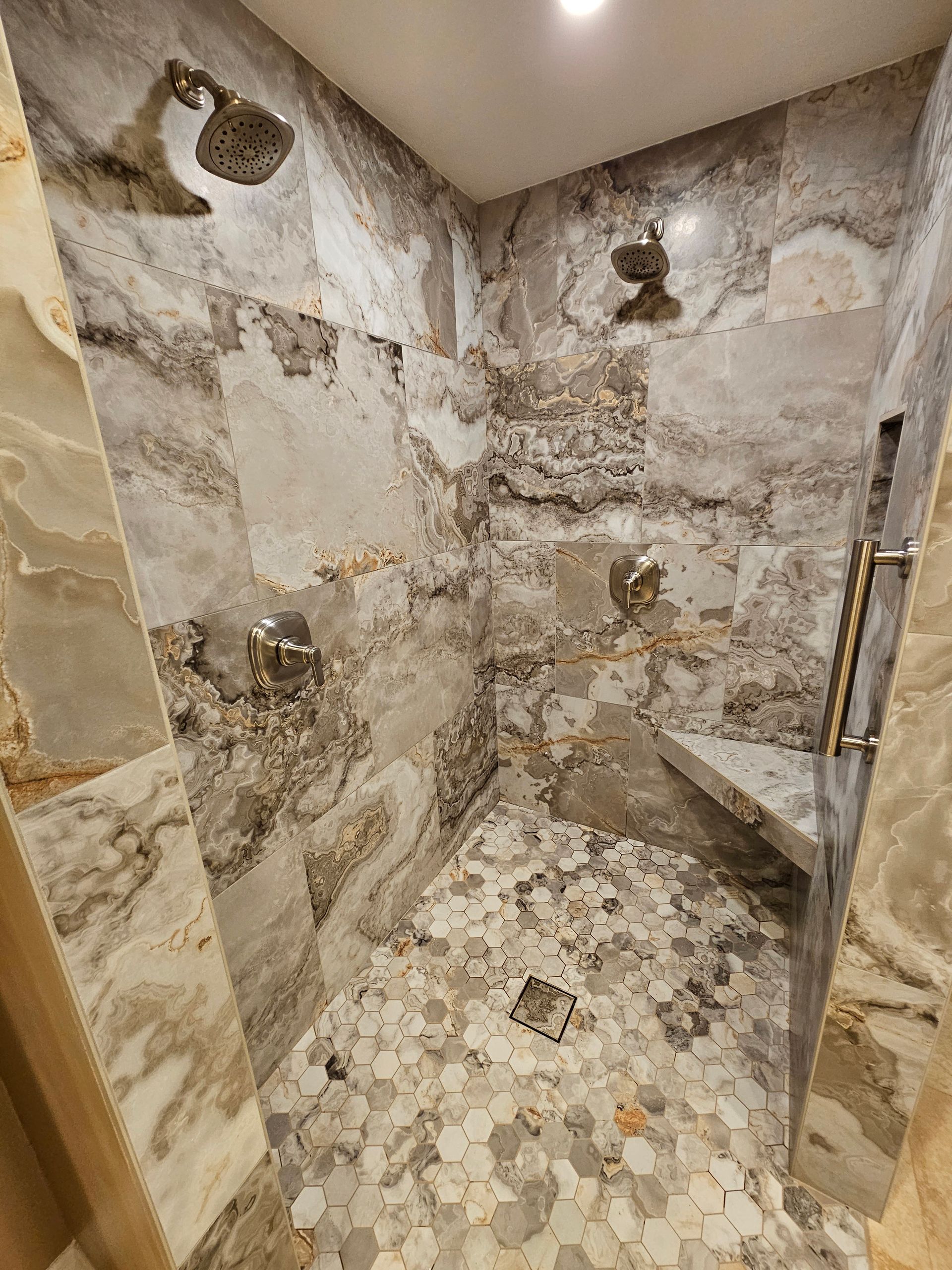Tiled shower with two shower heads, a built-in bench, and patterned stone walls and floor.