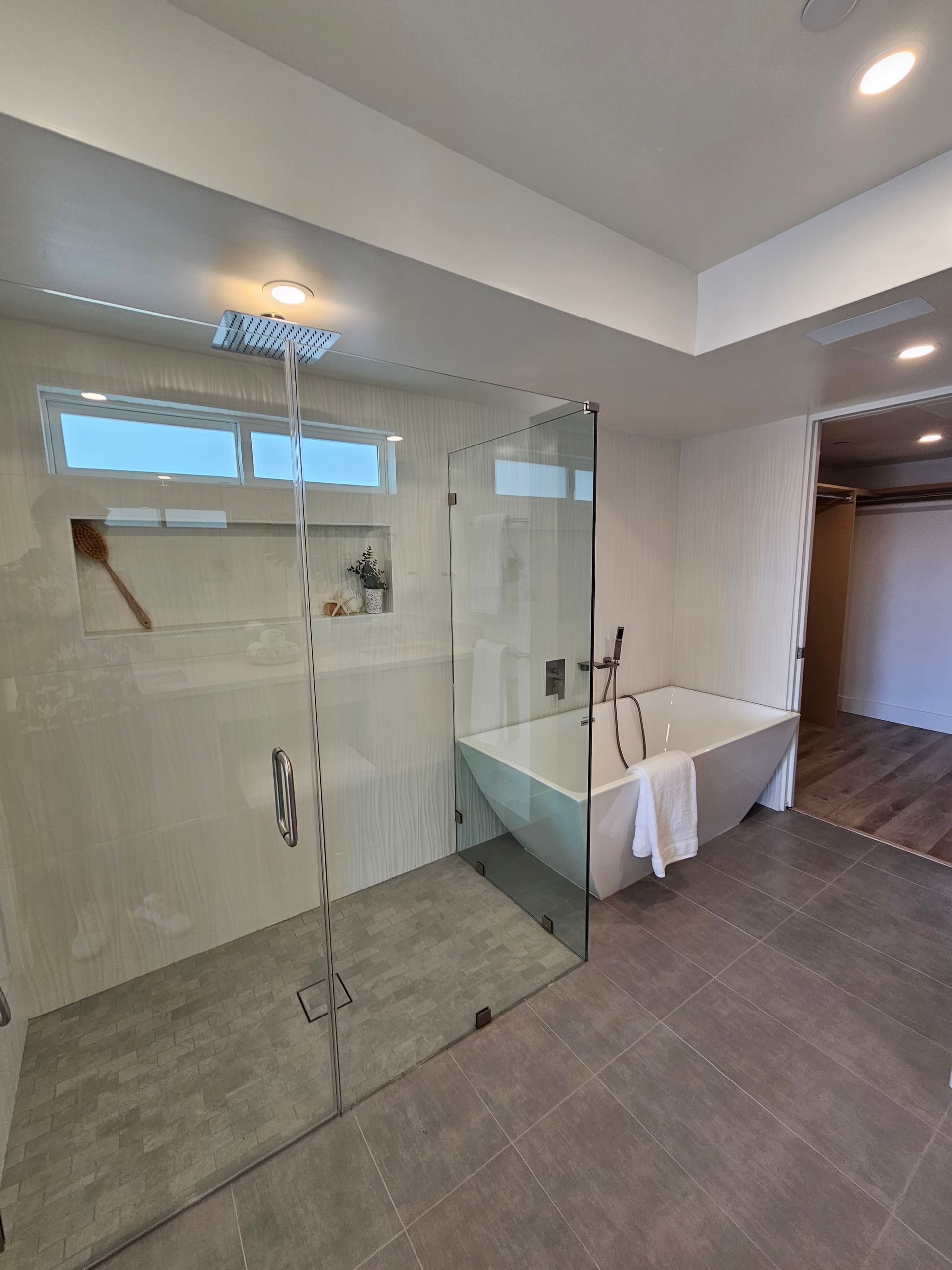Modern bathroom with a glass shower, white soaking tub, and gray tile floor.