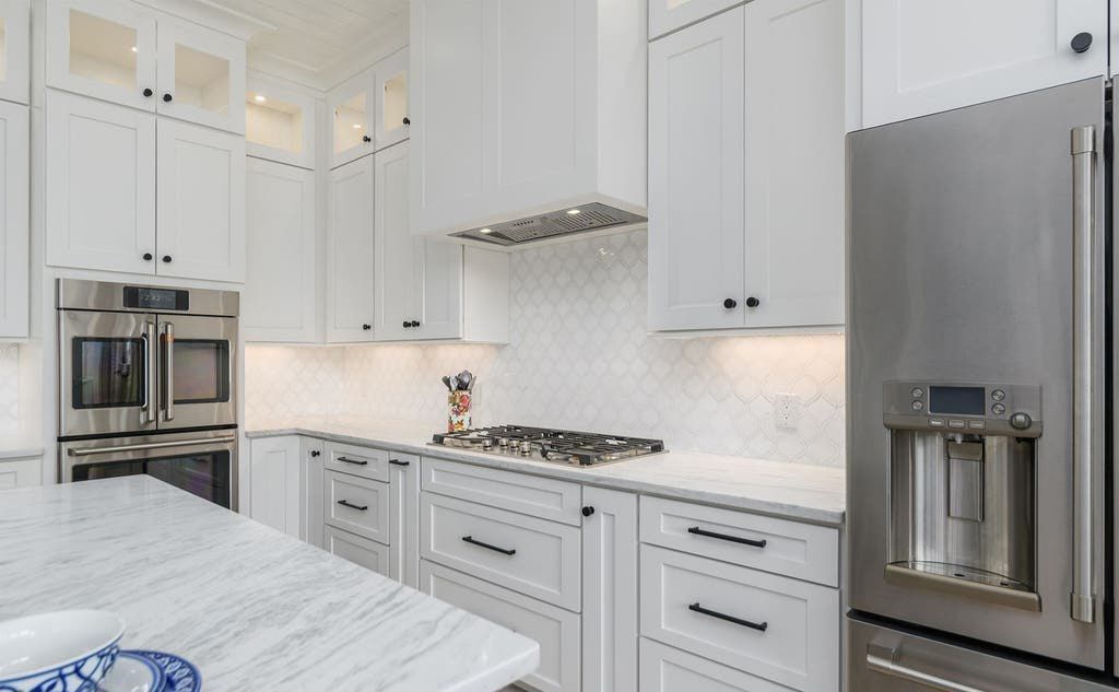 White kitchen with stainless steel appliances and cabinets, marble countertops.