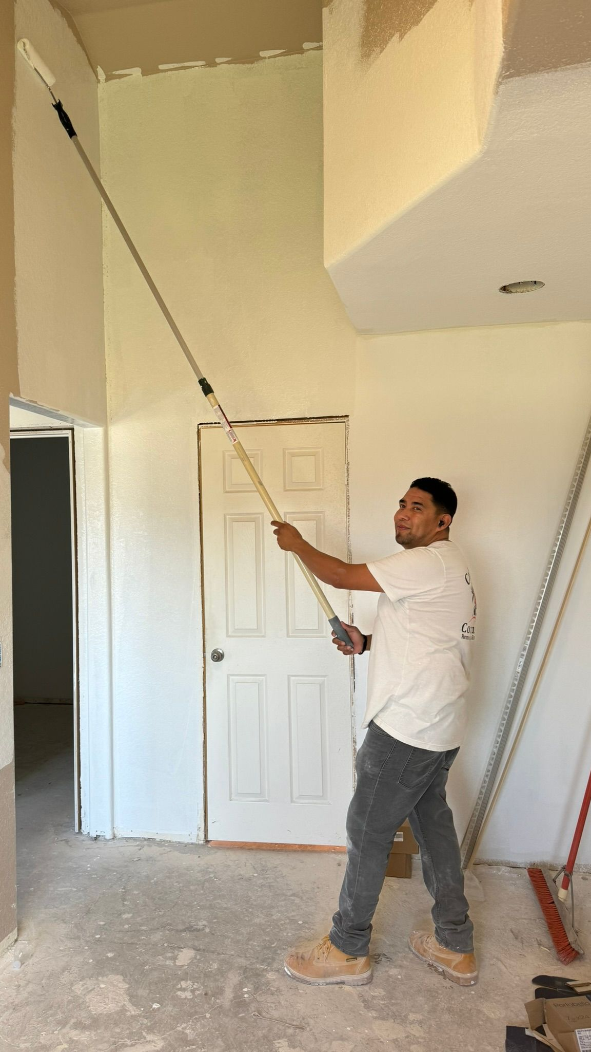 Man painting a high wall with an extension roller in a room under construction.